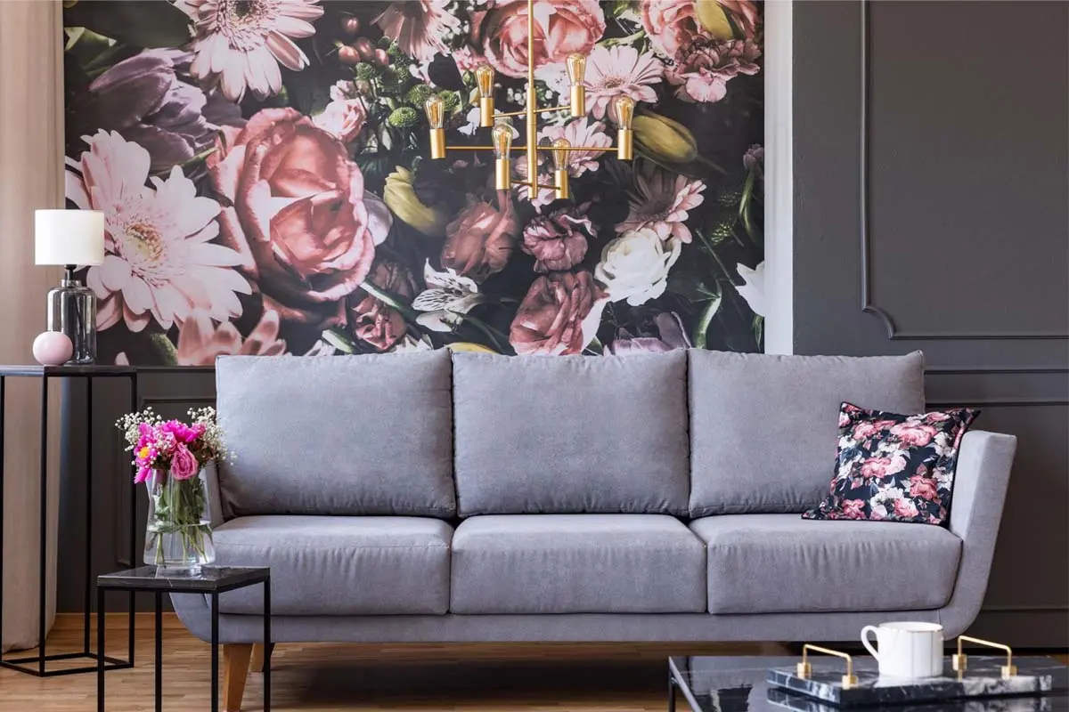 Living room with bold floral wallpaper, gray sofa, floral pillow, and decorative lighting creating a vibrant focal point.