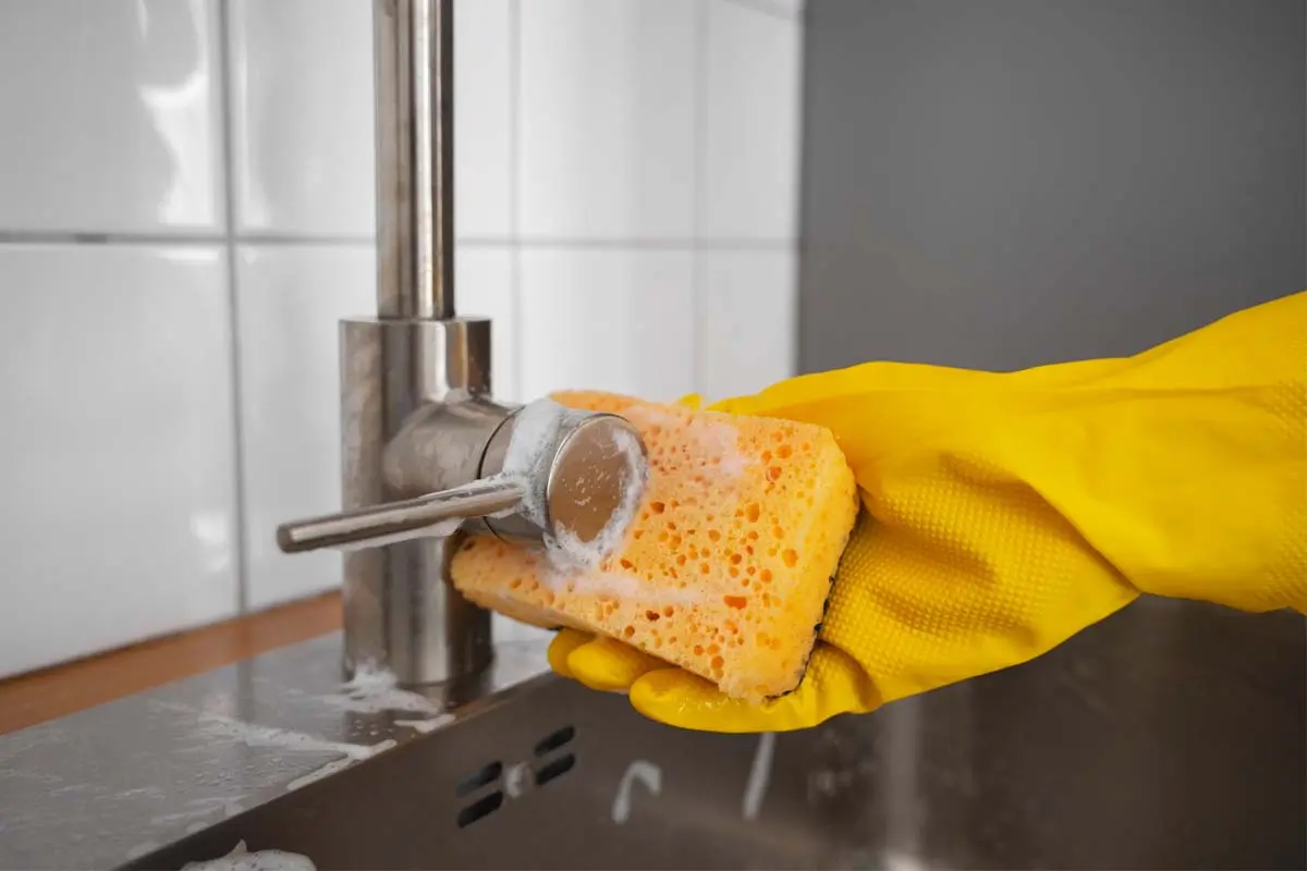 Scrubbing a faucet with a soapy sponge.