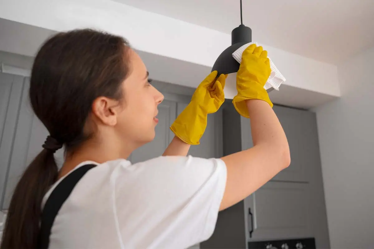A woman dusting light fixtures with gloves.