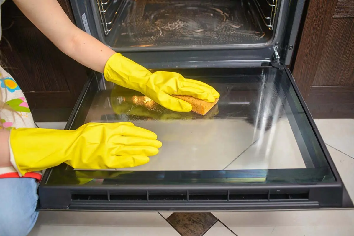 Oven door cleaning with protective gloves.