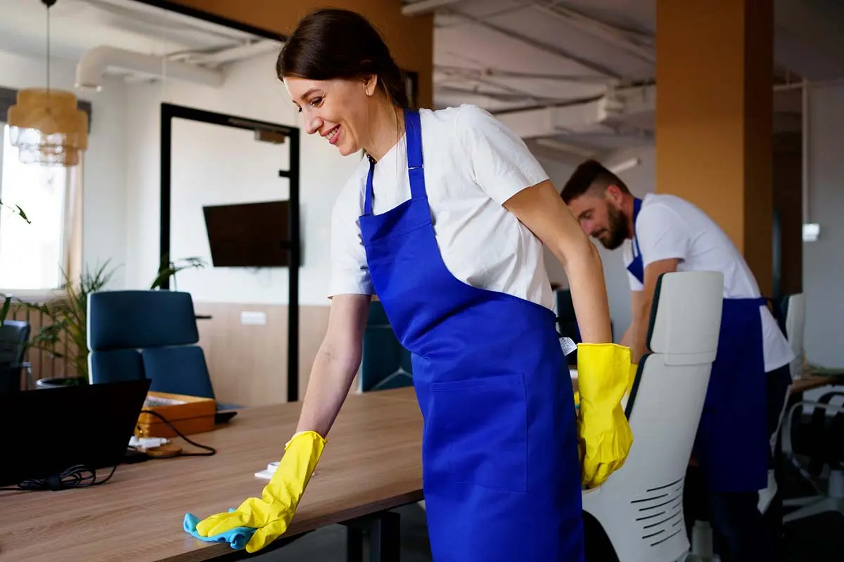 Cleaning team cleaning office desks in blue aprons.